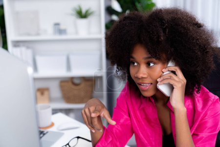 Afrikanerin im Gespräch mit Kollegin oder Freundin am Telefon und mit glücklichem Gesicht auf den Bildschirm starrend. Errungenschaften zur Förderung der Arbeitsplatzposition im Unternehmen mit dem Leben der guten Nachrichten. Geschmacksmacher.