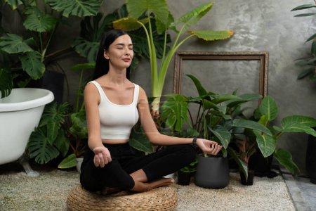 Téléchargez les photos : Jeune femme faisant du yoga matinal et de la méditation dans un jardin naturel avec des feuilles de plantes, profitant de la solitude et pratiquant des poses méditatives. Activité de pleine conscience et mode de vie sain. Blithe - en image libre de droit