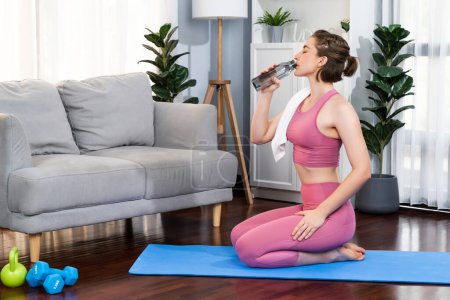 Photo for Athletic and sporty woman drinking water on fitness mat after finishing home body workout exercise session for fit physique and healthy sport lifestyle at home. Gaiety home exercise workout training. - Royalty Free Image