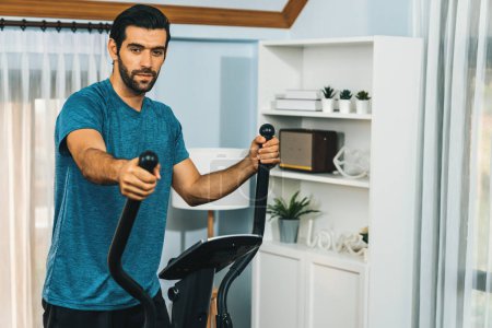 Photo for Athletic and sporty man running on elliptical running machine during home body workout exercise session for fit physique and healthy sport lifestyle at home. Gaiety home exercise workout training. - Royalty Free Image