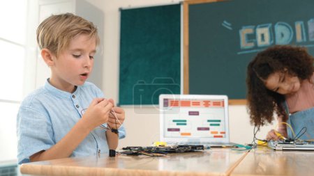 Photo for Girl standing while fixing electronic board by using screwdriver. American student and happy caucasian boy working together to inspect electric system. Curious children working on board. Pedagogy. - Royalty Free Image