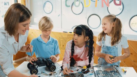 Photo for Young smart caucasian teacher teaching diverse students about electronic board. Multicultural children learn about digital electrical tool and fixing motherboard by using chips and wires. Erudition. - Royalty Free Image
