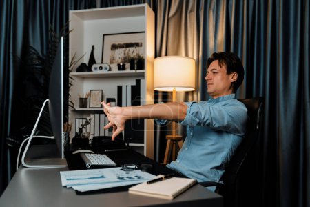 Photo for Sales manager working on desk with stretching arm up and down manner at night time at modern home office with monthly sales report for quarter presentation summary of profitable product. Pecuniary. - Royalty Free Image