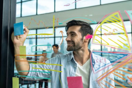 Photo for Portrait of young handsome businessman writing marketing idea by using colorful marker on glass wall with graph and mind map. Manager sharing idea or financial strategy. Business plan. Tracery. - Royalty Free Image