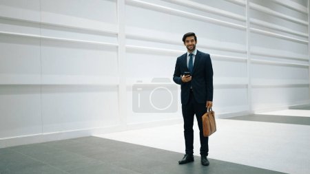 Smart manager looking at phone while standing at white background. Handsome male leader checking email or updated project and planing marketing strategy. while standing at white background. Exultant.