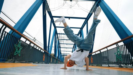 Photo for Professional break dancer perform street dance footstep at bridge. Asian hipster wear headphone while doing freeze pose. Break dancer, street dancer freestyle concept. Outdoor sport 2024. Sprightly. - Royalty Free Image