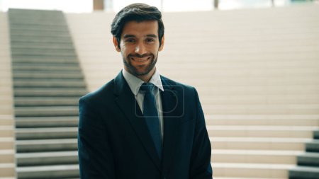 Téléchargez les photos : Portrait d'un homme d'affaires souriant regardant la caméra alors qu'il se tenait debout dans les escaliers. Gros plan de l'homme à succès souriant à la caméra tout en portant un costume d'affaires. Joyeux directeur exécutif regardez la caméra. Exultant. - en image libre de droit