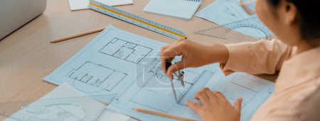 Photo for Professional architect drawing blueprint by using divider on the table with stationary and architectural document scatter around at architectural office. Closeup. Focus on hand. Delineation. - Royalty Free Image