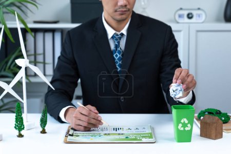 Photo for Businessman put paper waste on small tiny recycle bin in his office symbolize corporate effort on eco-friendly waste management by recycling for greener environment and zero pollution. Gyre - Royalty Free Image