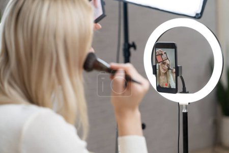 Photo for Rear view young woman making beauty and cosmetic tutorial video content for social media. Beauty blogger showing how to apply beauty care to audience or follower on camera screen. Blithe - Royalty Free Image