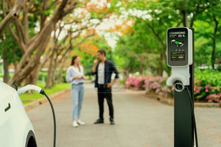 Photo for Focused EV car recharging battery on blurred background of lovey couple during autumnal road trip travel with electric vehicle recharging battery. Eco friendly travel on vacation during autumn. Exalt - Royalty Free Image