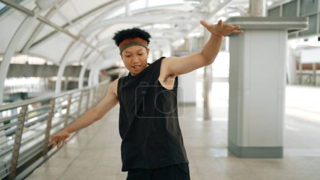 Foto de Bailarín guapo inteligente moviendo las manos mientras baila música hip hop. Profesional asiático hipster usando auriculares mientras camina a lo largo del pasillo con fondo borroso. Deporte al aire libre 2024. Rígidamente.. - Imagen libre de derechos