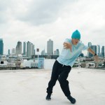 Caucasian B-boy dancer practicing street dancing at rooftop with city urban view. Motion shot of young man performing street dance by moving with hip -hop music. Outdoor sport 2024. Endeavor.