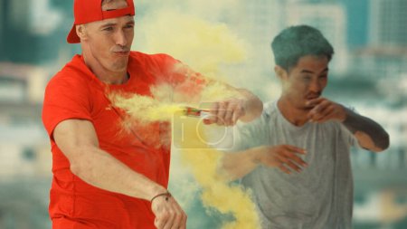 Photo for Portrait of caucasian hipster hold yellow smoke flare on roof top at building. Group of break dance practicing performance with sky scrapper Blurring background. Endeavor. - Royalty Free Image
