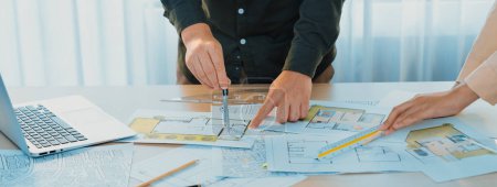 Photo for A cropped image of professional engineer using divider to measure blueprint at meeting table with blueprint, laptop and architectural equipment scatter around. Closeup. Delineation. - Royalty Free Image