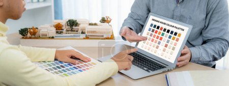 Photo for Professional architect presents color selection by using laptop displayed the color while female interior designer selects the curtain material. Creative working and teamwork concept. Variegated. - Royalty Free Image