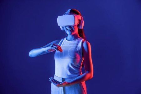 Photo for Female standing surrounded by neon light wear VR headset connecting metaverse, futuristic cyberspace community technology. Elegant woman using both hand interacting with virtual object. Hallucination. - Royalty Free Image
