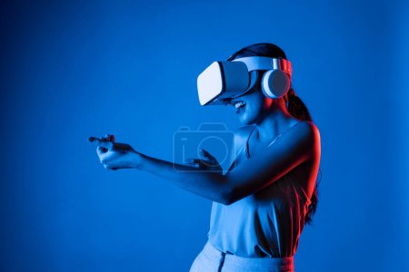 Photo for Smart female standing wearing VR headset connecting metaverse, future cyberspace community technology. Elegant woman using hands commanding virtual gun seriously playing shooting games. Hallucination. - Royalty Free Image