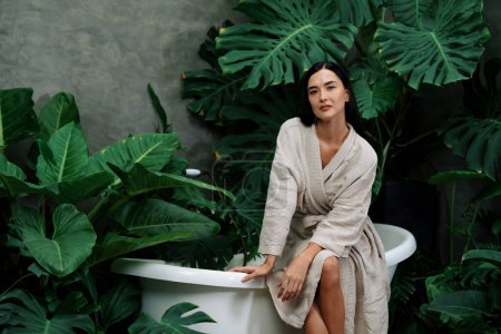 Photo for Tropical and exotic spa garden with bathtub in modern hotel or resort with young woman in bathrobe enjoying leisure and wellness lifestyle surrounded by lush greenery foliage background. Blithe - Royalty Free Image