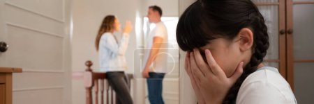 Photo for Stressed and unhappy young girl huddle in corner, cover her face while her parent arguing in background. Domestic violence at home and traumatic childhood develop to depression. Panorama Synchronos - Royalty Free Image