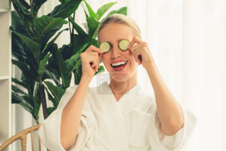 Photo for Woman holding slices of fresh cucumber and wearing bathrobe enjoying luxurious facial skincare spa in resort or hotel. Skin treatment for face and beauty care. Quiescent - Royalty Free Image