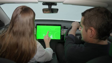 Photo for Holiday vacation road trip with environmental-friendly car concept. Eco-conscious young couple on driver seat holding blank copyspace green screen cars monitor for EV battery status. Exalt - Royalty Free Image
