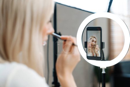 Photo for Rear view young woman making beauty and cosmetic tutorial video content for social media. Beauty blogger showing how to apply beauty care to audience or follower on camera screen. Blithe - Royalty Free Image