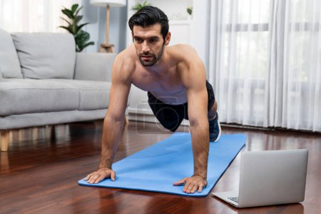 Photo for Athletic and sporty man doing pushup on fitness mat during online body workout exercise session for fit physique and healthy sport lifestyle at home. Gaiety home exercise workout training. - Royalty Free Image