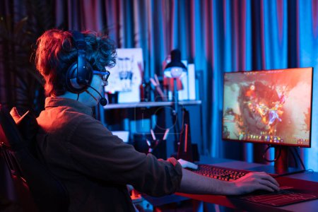 Photo for Host channel of young gaming streamer playing fighting Moba at battle arena game with multiplays team, wearing headphone on pc monitor with back side image at neon digital light modern room. Gusher. - Royalty Free Image