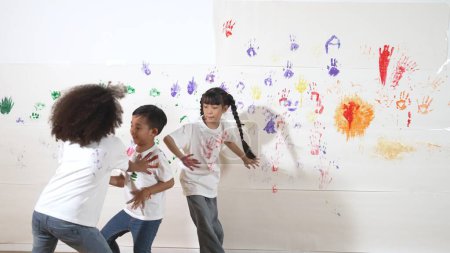 Photo for Playful children playing and running with colorful stained hand in front of white background. Funny happy multicultural students enjoy attending in art lesson. Creative activity concept. Erudition. - Royalty Free Image