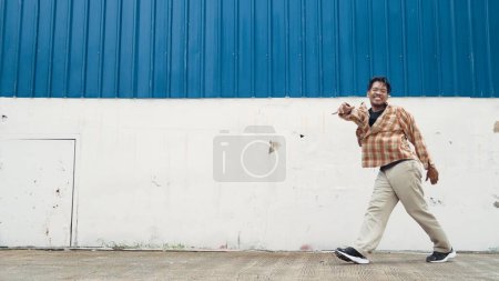 Téléchargez les photos : Chorégraphe drôle hispanique dansant dans le style hip hop. Jeune danseur heureux pause effectuer b-boy danse. Tournage en mouvement d'un homme drôle pratiquant la danse de rue. Sport de plein air 2024. La danse moderne. Endeavor. - en image libre de droit