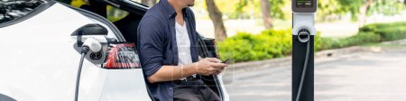 Mann nutzt Smartphone-Online-Banking-App, um im Urlaub im Nationalpark oder im Sommerwald an der Ladestation für Elektroautos zu bezahlen. Panorama Exalt