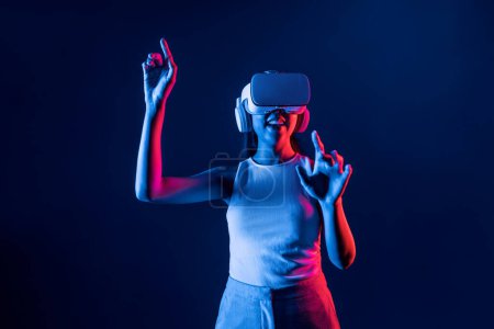 Photo for Smart female standing in cyberpunk neon light wear VR headset connecting metaverse, futuristic cyberspace community technology. Elegant woman use finger point generated virtual object. Hallucination. - Royalty Free Image