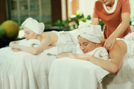 Téléchargez les photos : Un portrait de deux jeunes femmes séduisantes allongées sur le lit lors d'un massage du dos par un masseur professionnel en plein air entouré d'un environnement naturel paisible. Concept santé et beauté. Tranquillité. - en image libre de droit
