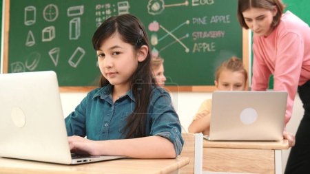 Photo for Smart asian girl looking at camera while coding engineering prompt. Multicultural student learning about generated AI while teacher teaching about system or checking classwork at STEM class. Pedagogy. - Royalty Free Image