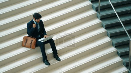 Photo for Top view business man celebrate successful project while sitting at stairs. Smart project manager getting new gob, getting promotion, increasing sales while calling friends by using laptop. Exultant. - Royalty Free Image