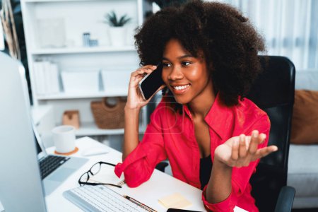 Afrikanerin im Gespräch mit Kollegin oder Freundin am Telefon und mit glücklichem Gesicht auf den Bildschirm starrend. Errungenschaften zur Förderung der Arbeitsplatzposition im Unternehmen mit dem Leben der guten Nachrichten. Geschmacksmacher.
