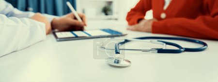 Photo for Focused stethoscope on office desk with blurred background of patient attending to doctor appointment at clinic or hospital discussing medical treatment or examining symptoms. Panorama Rigid - Royalty Free Image