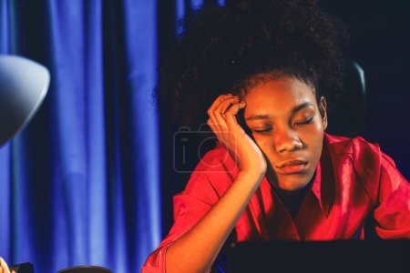 Erschöpfte und schläfrige junge afrikanische Geschäftsfrau macht ein Nickerchen auf dem Schreibtisch im Home Office. Konzept des Denkens eine Menge Projekte bis zum Schlafen zwischen unfertigen Online-Arbeit. Geschmacksmacher.