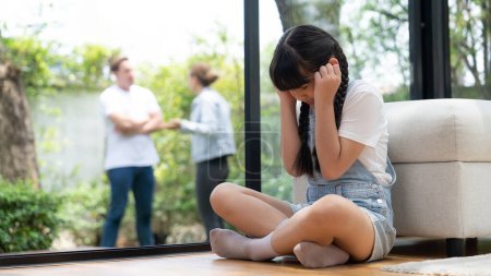 Photo for Stressed and unhappy young girl huddle in corner, cover her ears blocking sound of her parent arguing in background. Domestic violence at home and traumatic childhood depression. Panorama Synchronos - Royalty Free Image