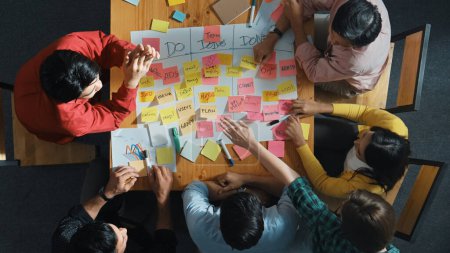 Photo for Top view of people writing and making scrum task board while writing marketing and planning strategy at colorful sticky notes. Smart team manage work performance by using kanaban board. Convocation. - Royalty Free Image