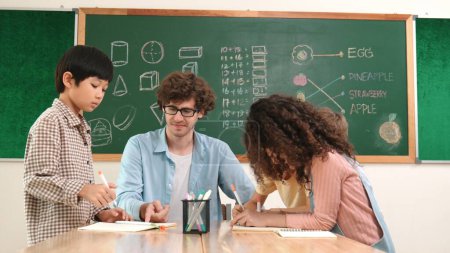 Photo for Smart teacher explain idea while diverse children drawing mind map while group of diverse student working together to do class work. Attractive instructor teaching and talking about working. Pedagogy. - Royalty Free Image