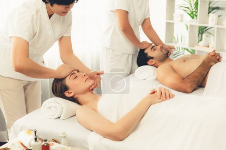 Téléchargez les photos : Couple caucasien profiter relaxant anti-stress massage de la tête et choyer beauté du visage loisirs de la peau dans dayspa lumière moderne ambiant au complexe de luxe ou un salon de spa de l'hôtel. Tranquillité - en image libre de droit