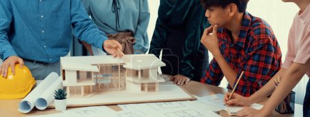 Photo for Architect team analysis and brainstorming about house construction at meeting table with house model, blueprint and architectural equipment scatter around. Creative design and teamwork. Burgeoning. - Royalty Free Image