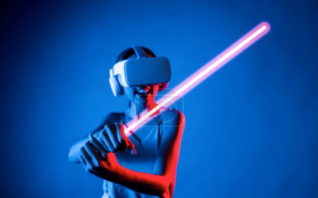 Photo for Smart female standing wearing VR headset connecting metaverse, future cyberspace community technology. Elegant woman firmly holding laser saber seriously while play sword-fighting game. Hallucination. - Royalty Free Image