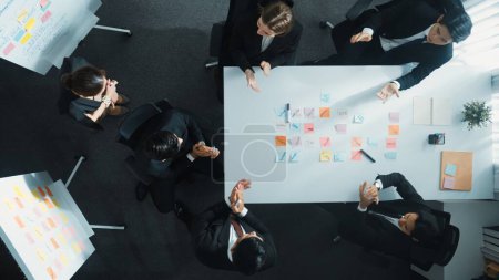 Photo for Top down aerial view of business group sharing and brainstorming idea by using sticky notes at meeting room. Investor writing marketing strategy on board while receive note from manager. Directorate. - Royalty Free Image