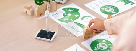 Photo for Environmental documents and a windmill model representing the use of clean energy are scattered on the table during a green business discussion about investing in clean energy. Closeup. Delineation. - Royalty Free Image