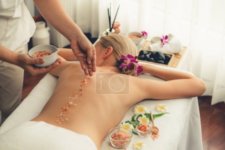 Photo for Woman customer having exfoliation treatment in luxury spa salon with warmth candle light ambient. Salt scrub beauty treatment in health spa body scrub. Quiescent - Royalty Free Image