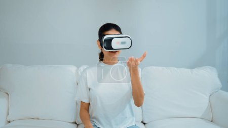 Foto de Mujer joven que usa gafas VR de realidad virtual en casa para vivir una experiencia de compra en línea. La innovación de realidad virtual VR optimizada para el estilo de vida de entretenimiento digital femenino. - Imagen libre de derechos