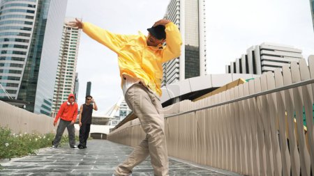 Happy hipster perform break dance while friend moving to music together. Handsome cool street dancer walking at camera while perform hip hop footstep. Modern lifestyle. Outdoor sport 2024. Sprightly.